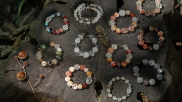 Handmade crystal bracelet being assembled on a wooden worktable with scattered beads and tools, showing care, texture, and intentional jewelry design.