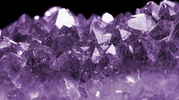 Raw amethyst crystal cluster on a soft pink background, showing rich purple facets and natural texture for modern crystal jewelry.