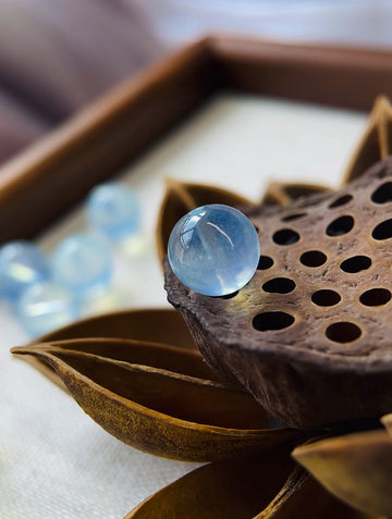 A close-up of an Aquamarine crystal bead resting on a dried lotus pod, symbolizing calm energy, clarity, and emotional healing in natural light 